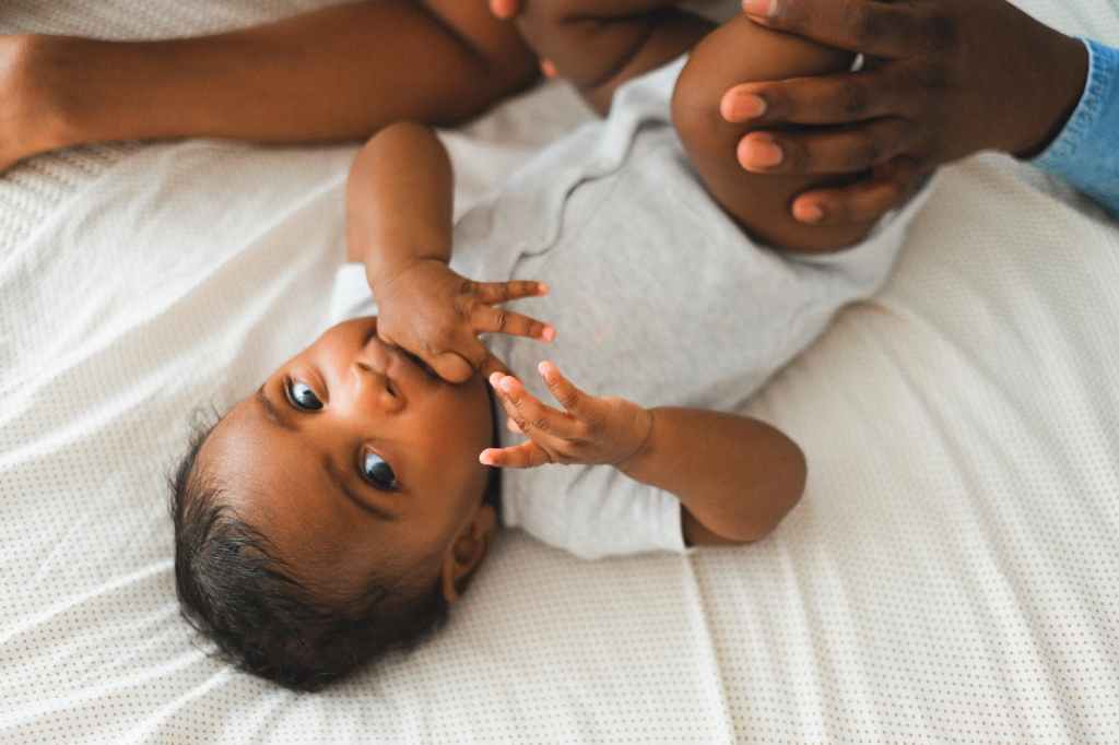 a baby in white onesie lying on the bed